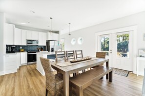 A modern kitchen with white cabinets, a wooden dining table, and a built-in oven.