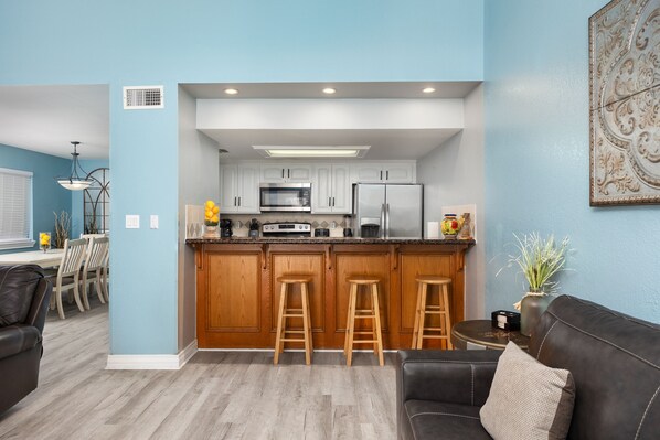 A modern kitchen with white cabinets, a stainless steel refrigerator, and wooden stools.