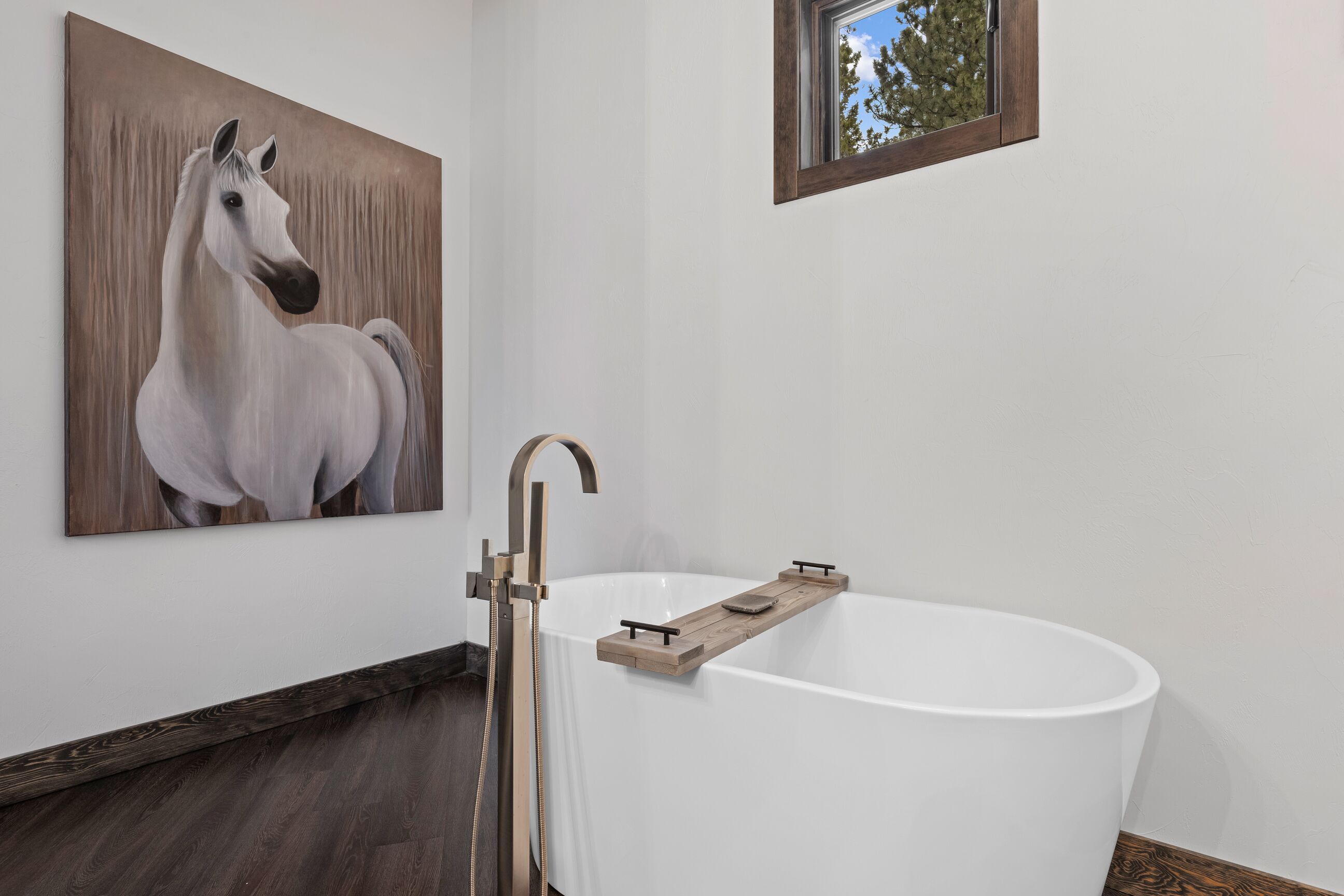 Ein modernes Badezimmer mit einer weißen Badewanne, einem Holzregal und einem Bild von einem Pferd an der Wand.