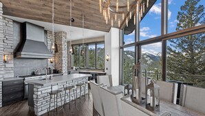 A modern kitchen with a large island, bar stools, and a view of mountains through large windows.