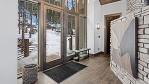 A modern interior with large glass doors leading to a snowy outdoor area, a bench, and a stone wall with a bear painting.