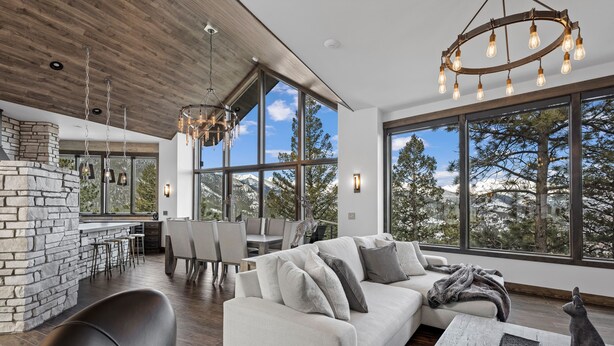 A modern interior with a stone fireplace, a large sofa, and a dining area with a view of trees and mountains.