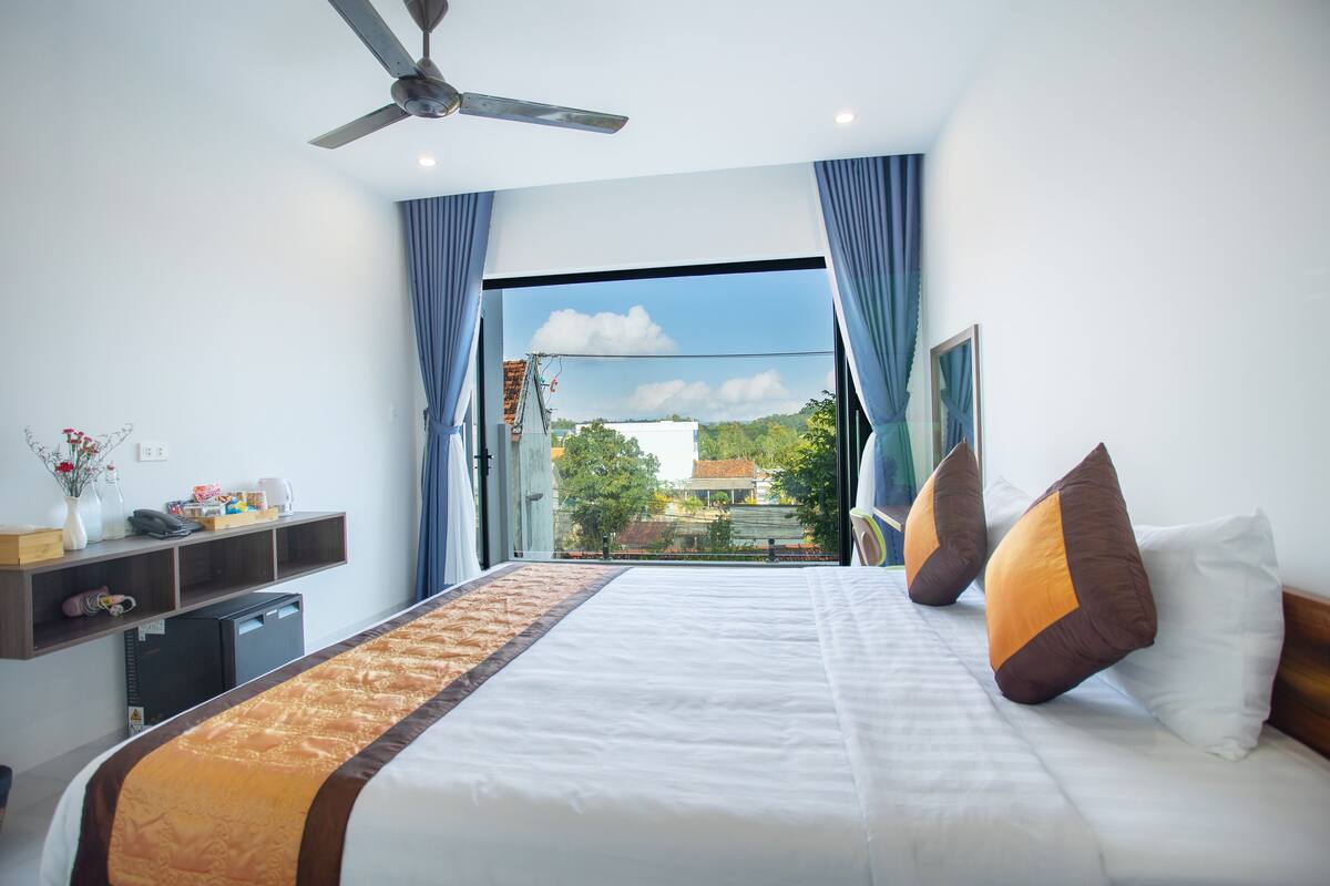 Une chambre d’hôtel avec un lit, un ventilateur de plafond, une fenêtre avec des rideaux et une vue sur l’extérieur.