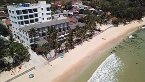 Ein Küstenhotel mit mehreren Gebäuden, einem Sandstrand und Palmen.