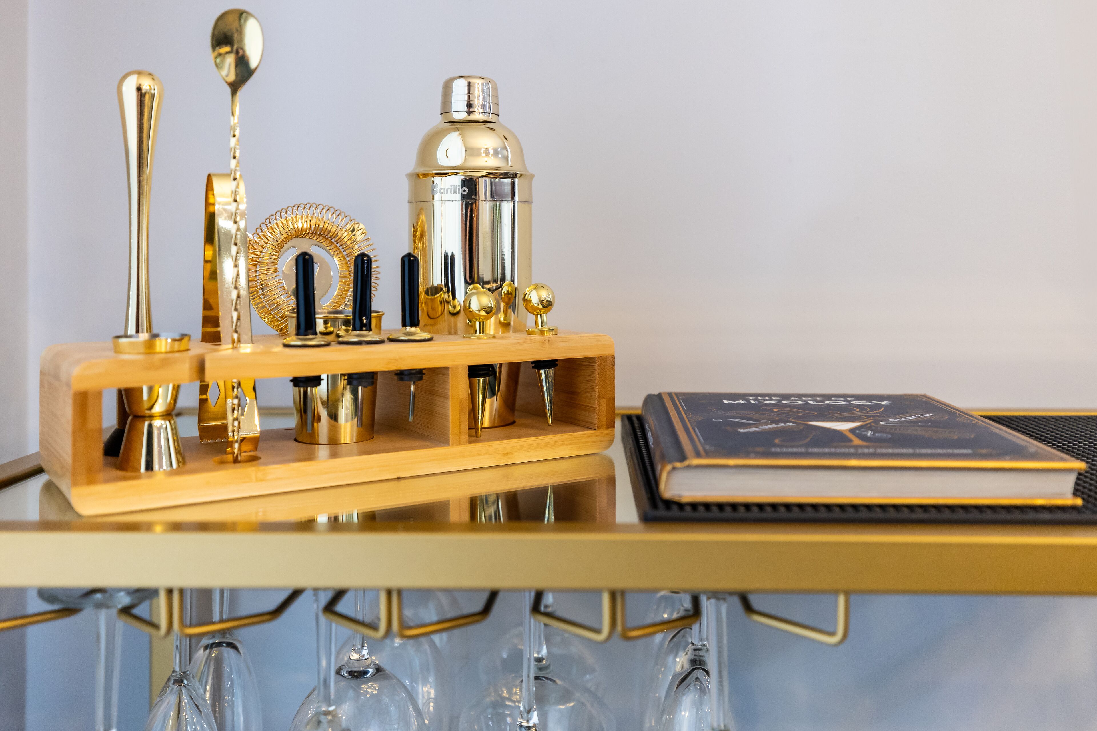A bar setup with a cocktail shaker, jigger, and other bartending tools on a wooden tray.