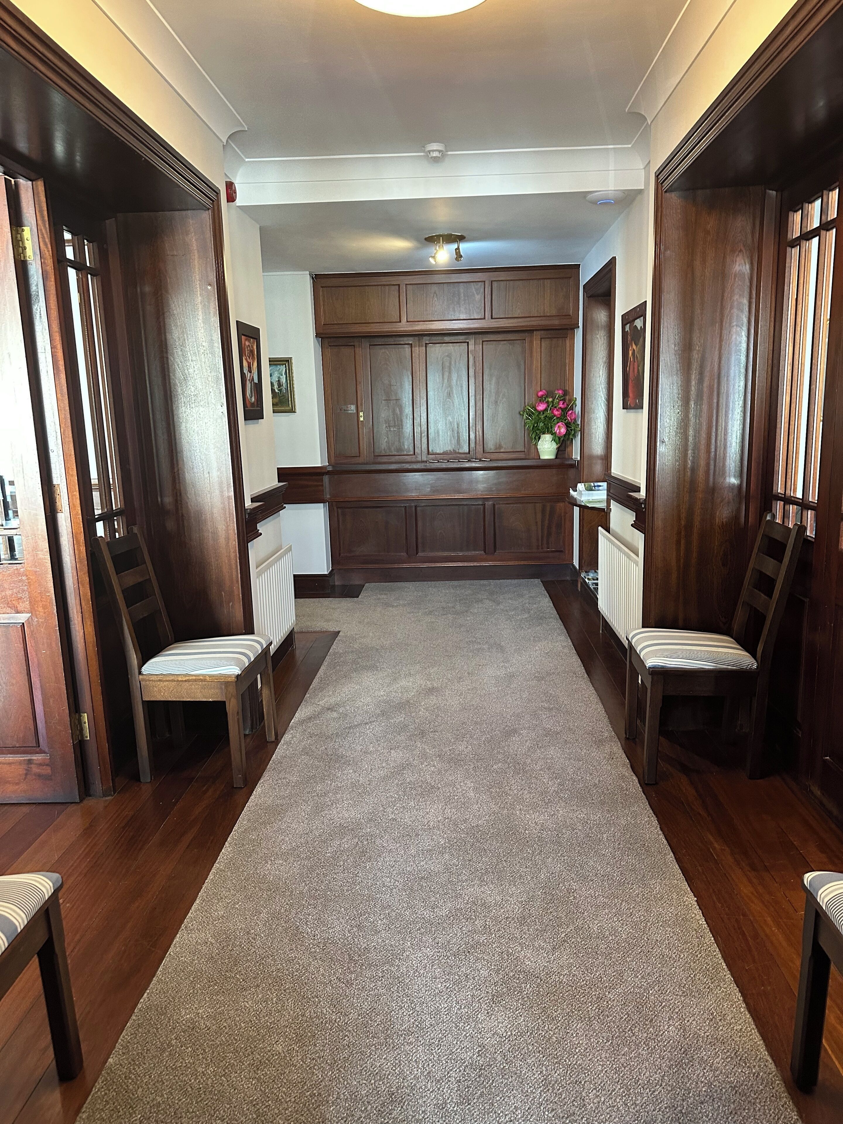 A hallway with wooden paneling, a carpet, and two chairs.