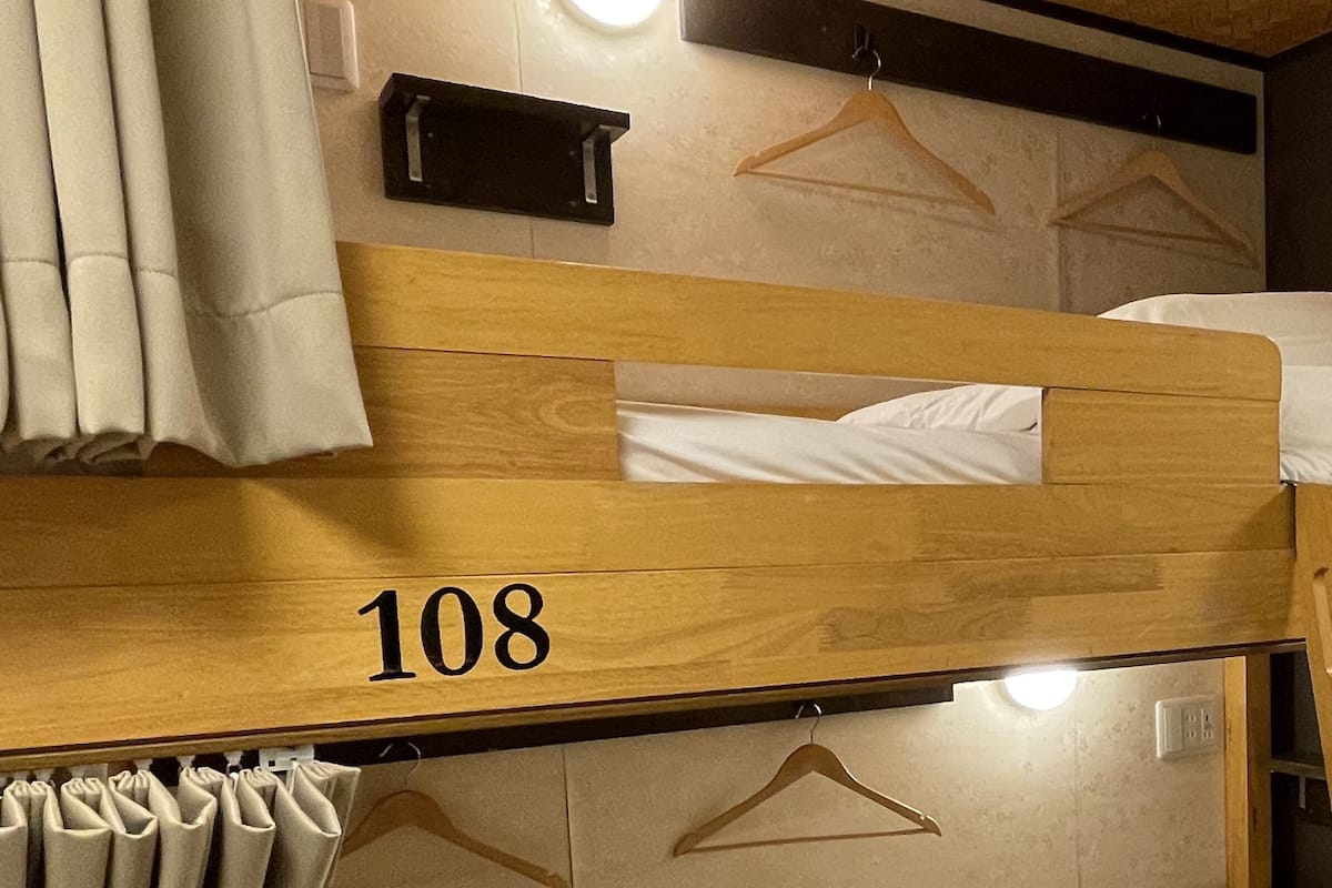 Une chambre avec un lit superposé, le numéro « 108 » étant inscrit sur la tête de lit, une suspension au plafond et une petite étagère au-dessus du lit.