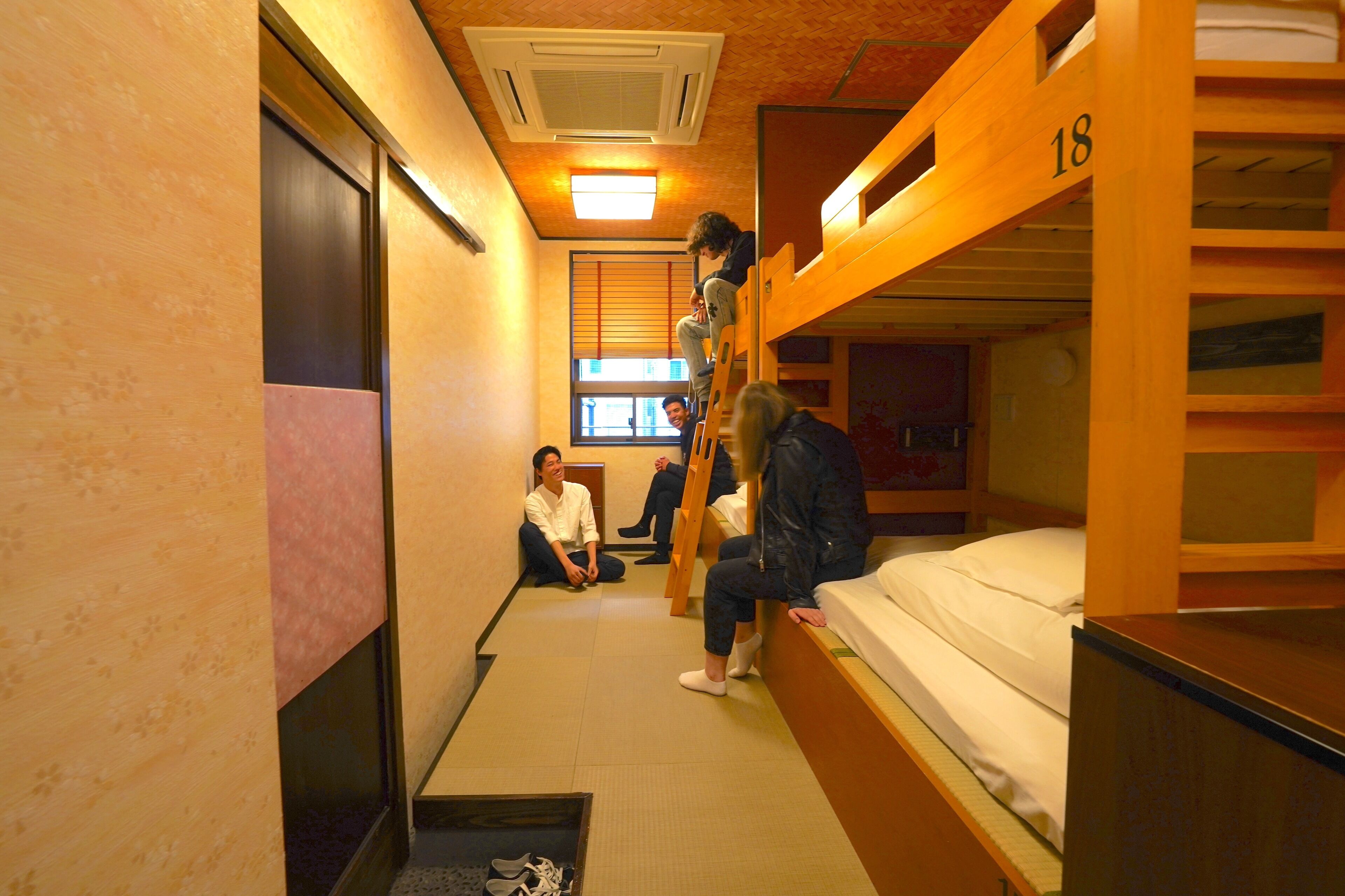 A dormitory room with bunk beds, a window with blinds, and a door.