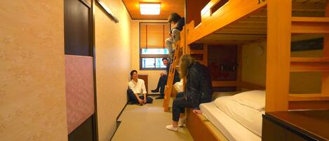 A dormitory room with bunk beds, a window with blinds, and a door.