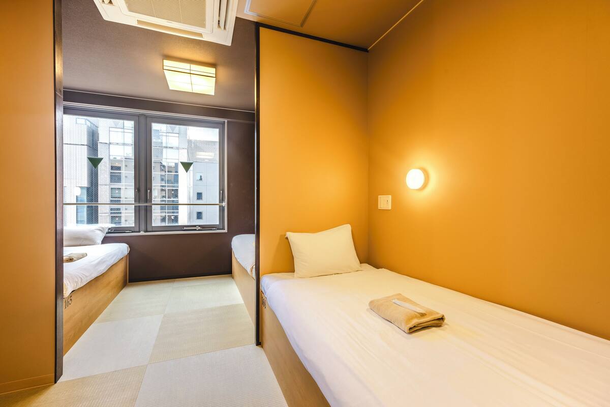 Une chambre d’hôtel de taille réduite, avec un lit simple, une fenêtre donnant sur la ville et un petit coin salon.