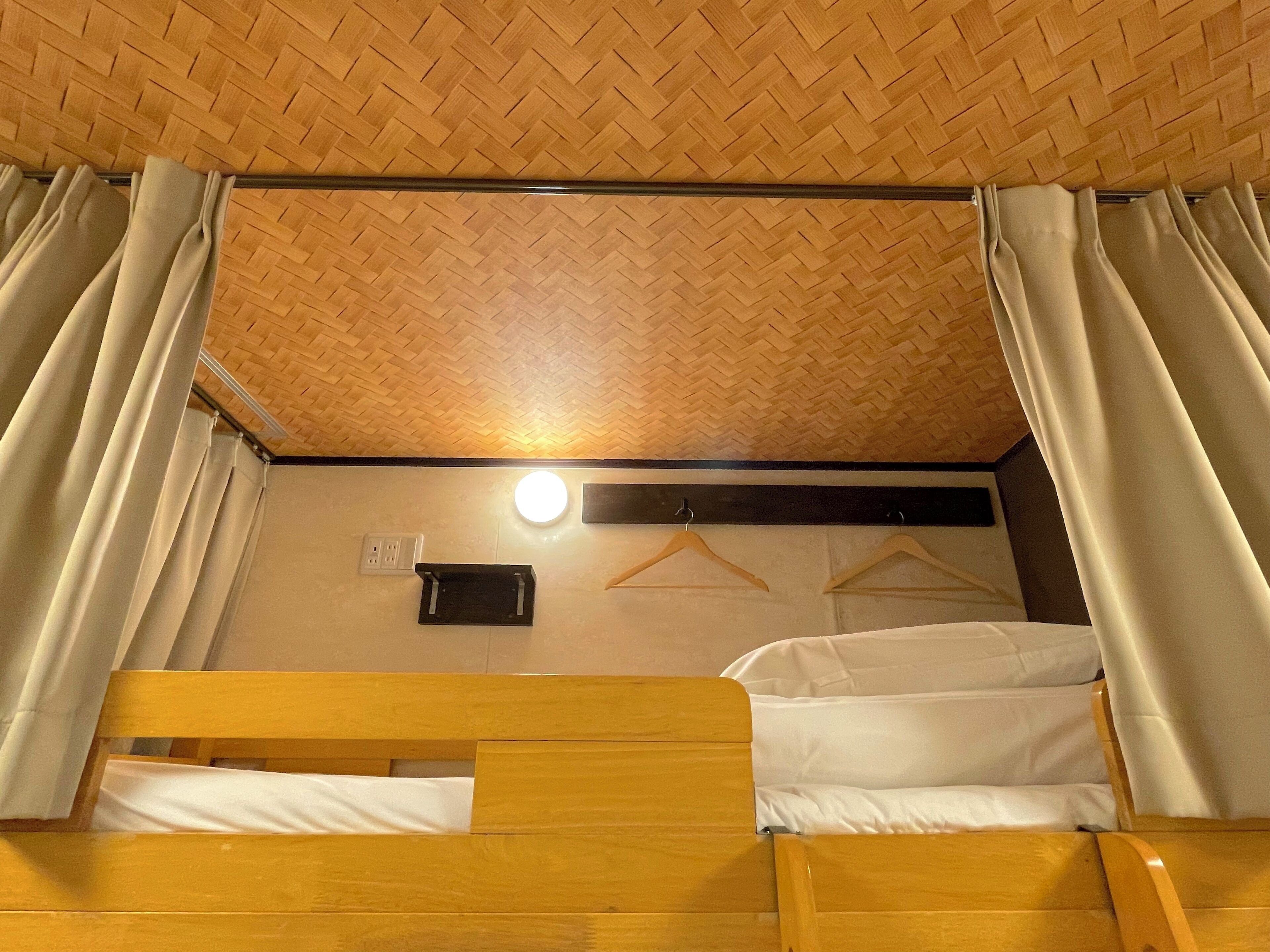 A bunk bed room with a wooden ceiling, a wall-mounted light, and a coat rack.
