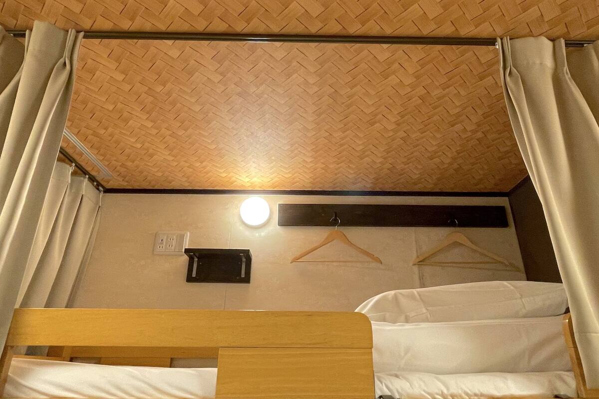 Une chambre avec un lit superposé, un plafond en bois, une lampe fixée au mur et une prise de courant.