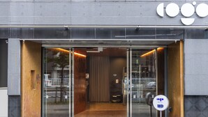 A modern building entrance with glass doors, a metal frame, and a sign with a logo. - Cogo Ryogoku (Tokyo)