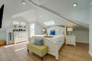 A bedroom with a sloped ceiling, a bed with white headboard, a bedside table, a nightstand, a bench, and a dresser.