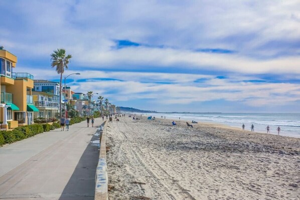 A beach with a paved walkway, palm trees, and buildings along the shore.