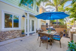 A patio with a table and chairs, a blue umbrella, and a stone wall.
