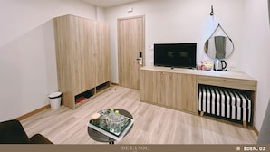 Una habitación moderna y bien iluminada con muebles de madera, un televisor de pantalla plana, un espejo y una pequeña zona de kitchenette.