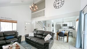 A spacious living room with a large black leather sofa, a glass coffee table, and a dining area with a wooden table and chairs. A kitchen is visible in the background with modern appliances. - Pocono Mountain Dream House with hot tub (Tobyhanna)