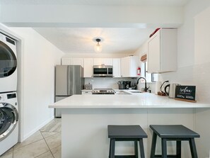 Una cocina moderna con armarios blancos, electrodomésticos de acero inoxidable, una isla central con taburetes y una lámpara colgante.