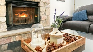 A cozy living room with a stone fireplace, a decorative tray with a candle, pine cones, and a potted plant. - Pocono Mountain Dream House with hot tub (Tobyhanna)