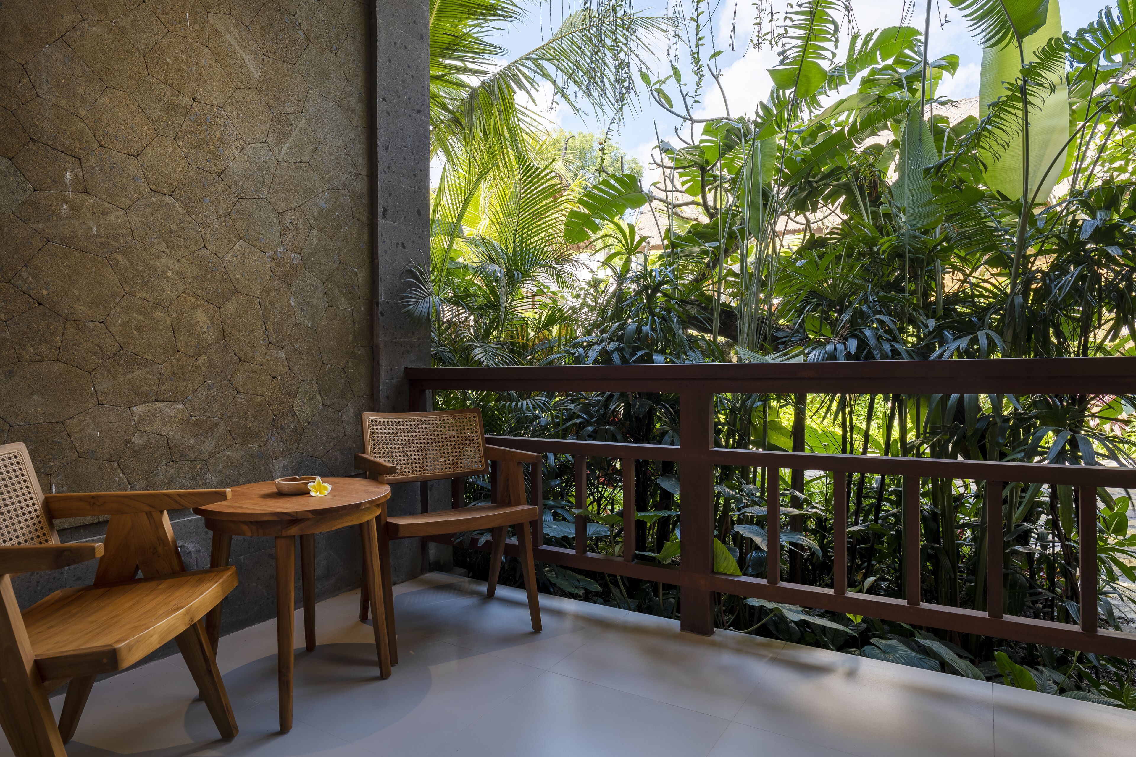 A balcony with wooden furniture and a view of lush tropical plants.