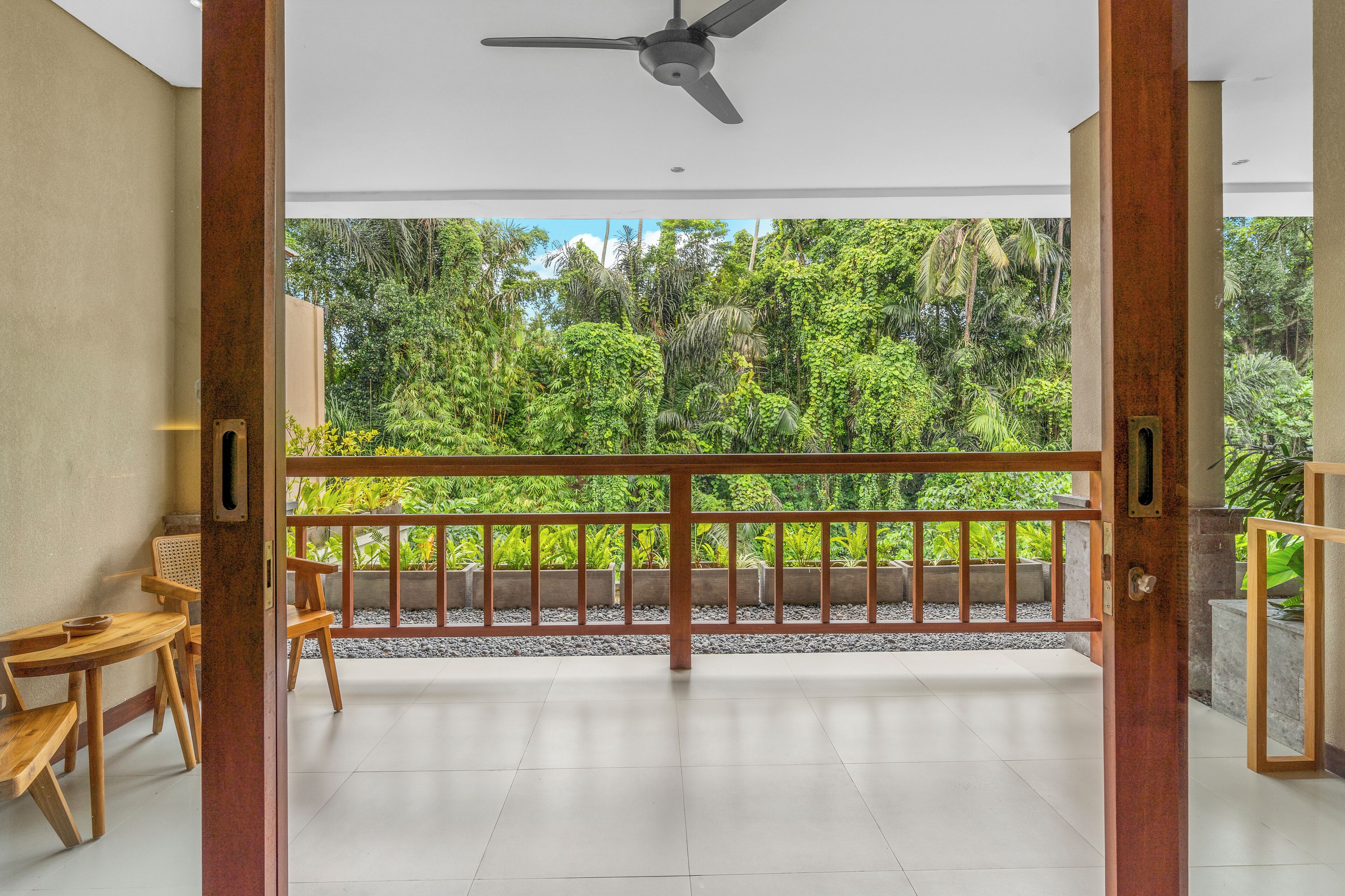 Ein Balkon mit Blick auf üppiges Grün, Holzmöbel und einem Deckenventilator.
