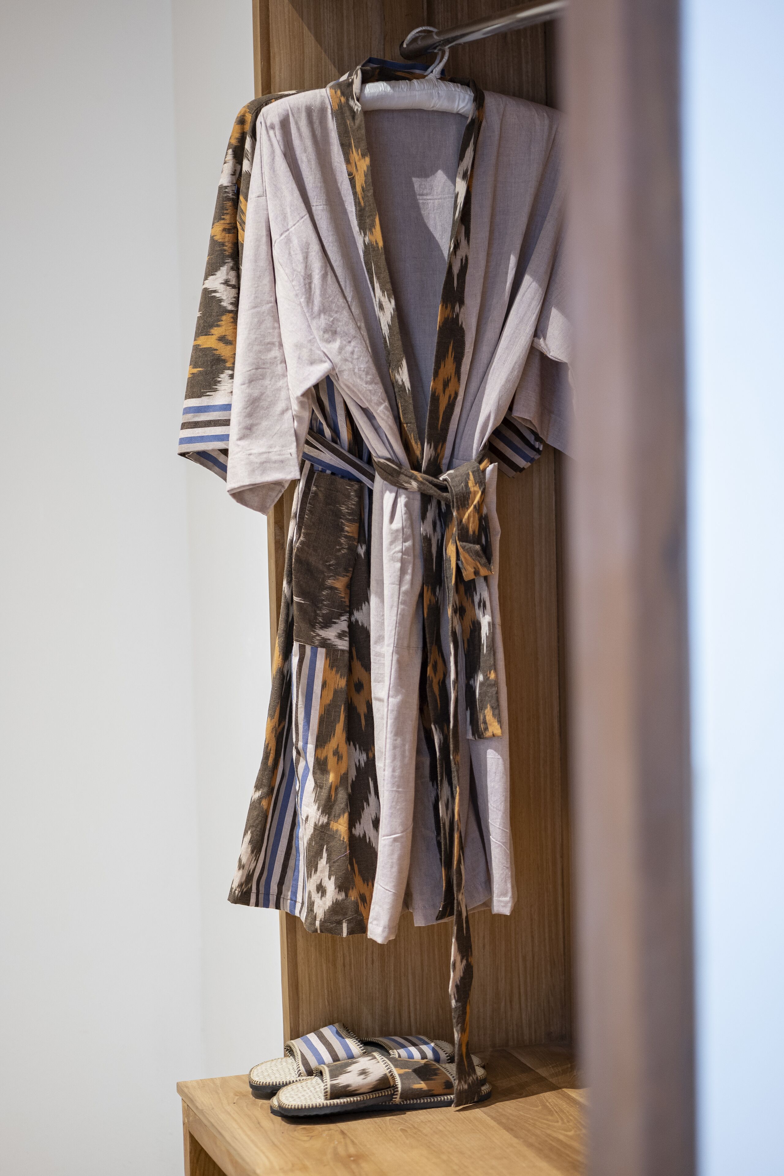 A wooden shelf with a pair of slippers and a robe with a leaf pattern.