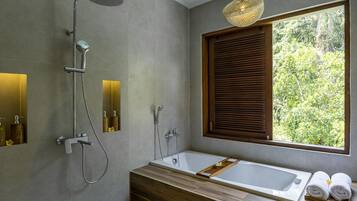A modern bathroom with a large bathtub, a showerhead, and a window with blinds.