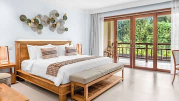 Een ruime slaapkamer met een groot bed, een houten bankje en uitzicht op weelderige begroeiing door een glazen schuifdeur.