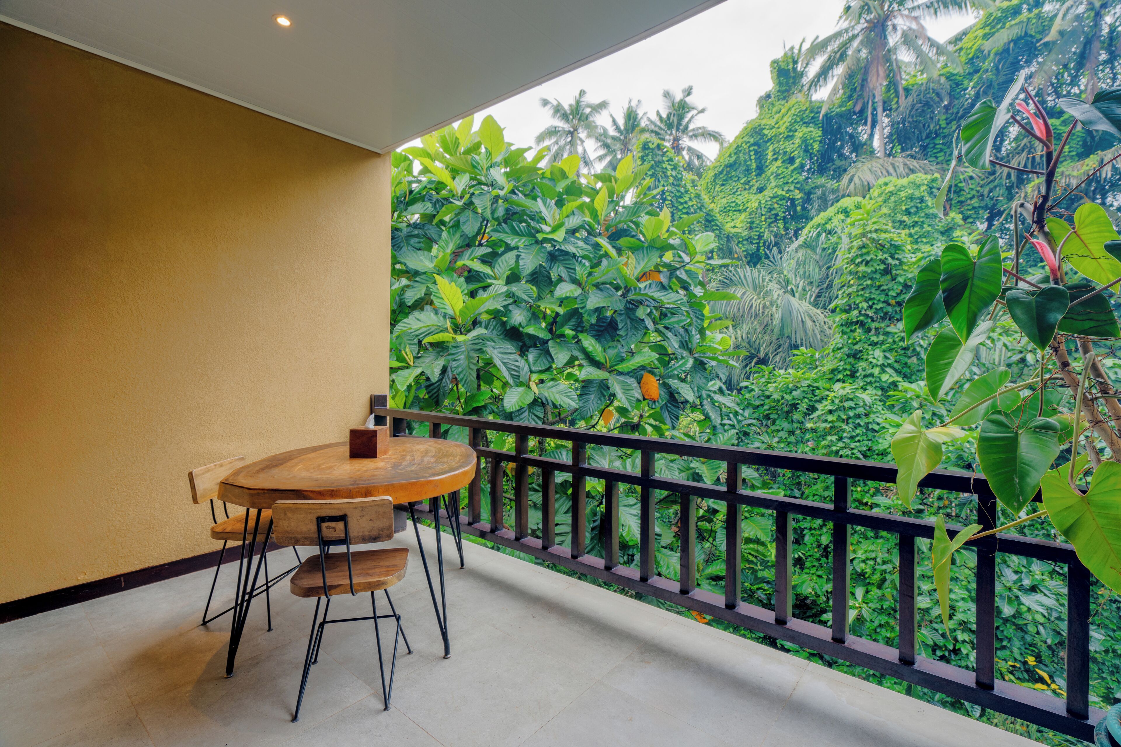 A balcony with a wooden table and chairs, surrounded by lush tropical vegetation and a view of dense greenery.