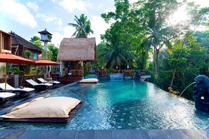 A pool area with lounge chairs and umbrellas, surrounded by lush greenery and a traditional thatched-roof structure. - Vije Boutique Resort & Spa (Ubud)