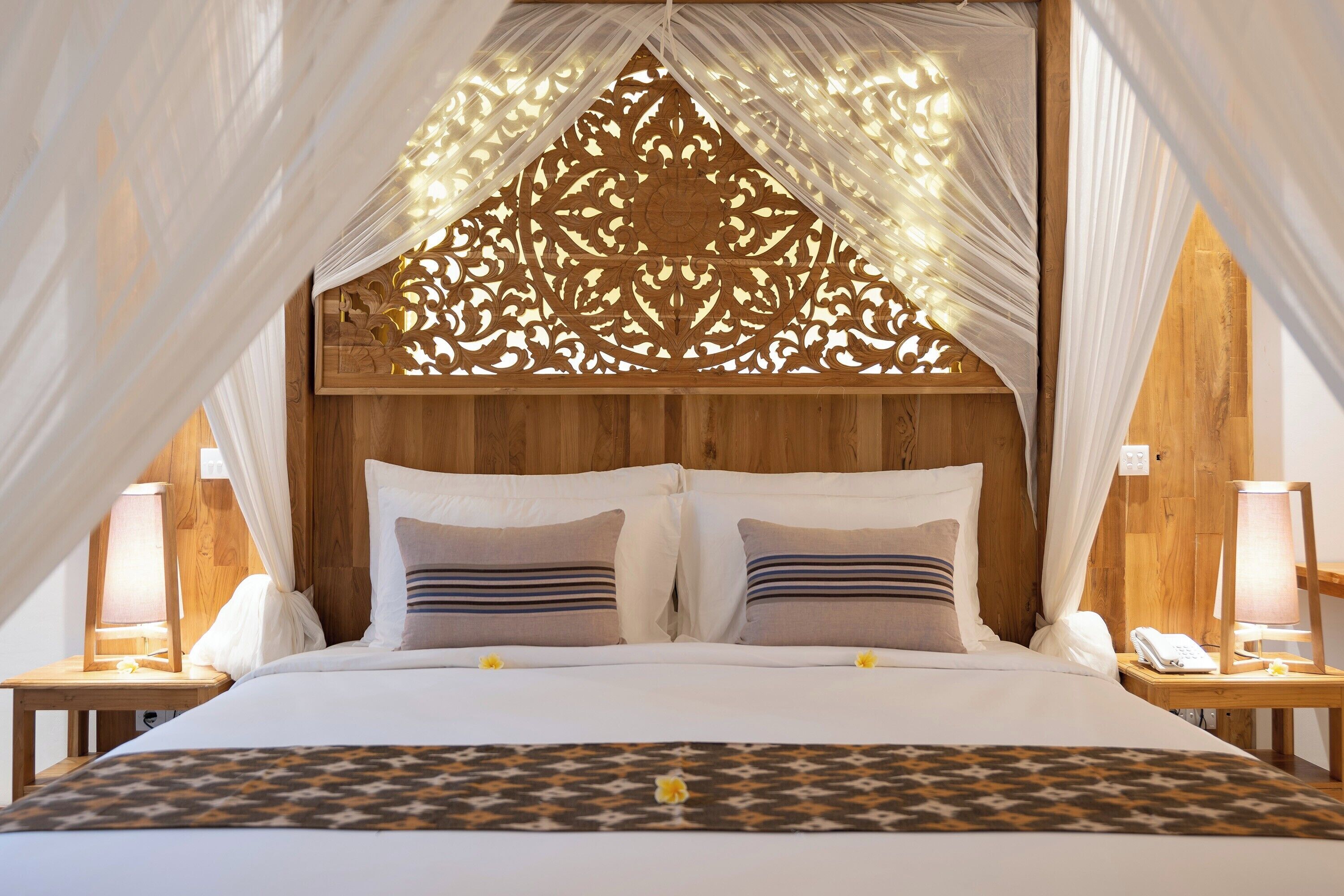 A bed with a canopy, wooden headboard, and bedside lamps.