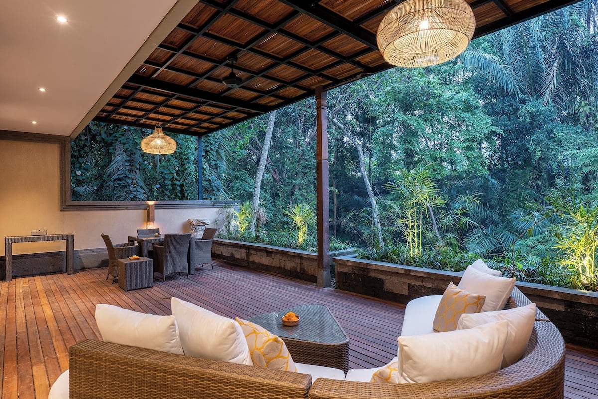 A spacious outdoor deck with wicker furniture and a view of dense tropical foliage.