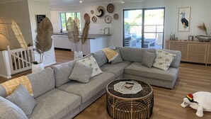 A modern living room with a grey sectional sofa, a round woven coffee table, and a white stuffed toy.