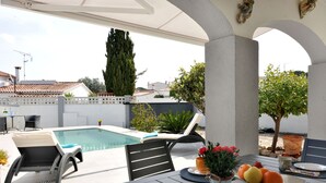 Zona de piscina amb taula, cadires i un plat de fruita.