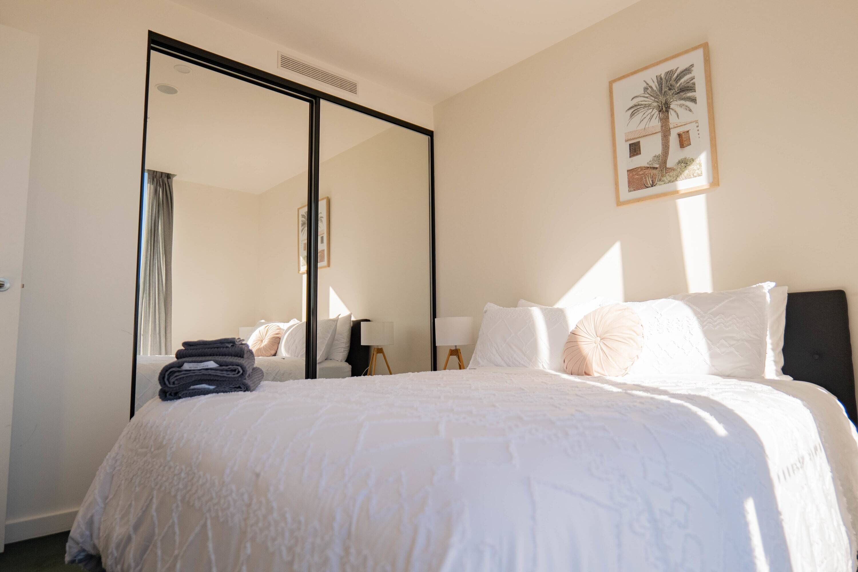 Ein Hotelzimmer mit einem großen Bett, einem Spiegel, einem gerahmten Bild an der Wand und einem Fenster mit Vorhängen.