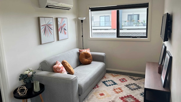 A modern living room with a grey sofa, two cushions, a patterned rug, and artwork on the wall. - Peaceful Coombs Apartment for Families (Coombs)