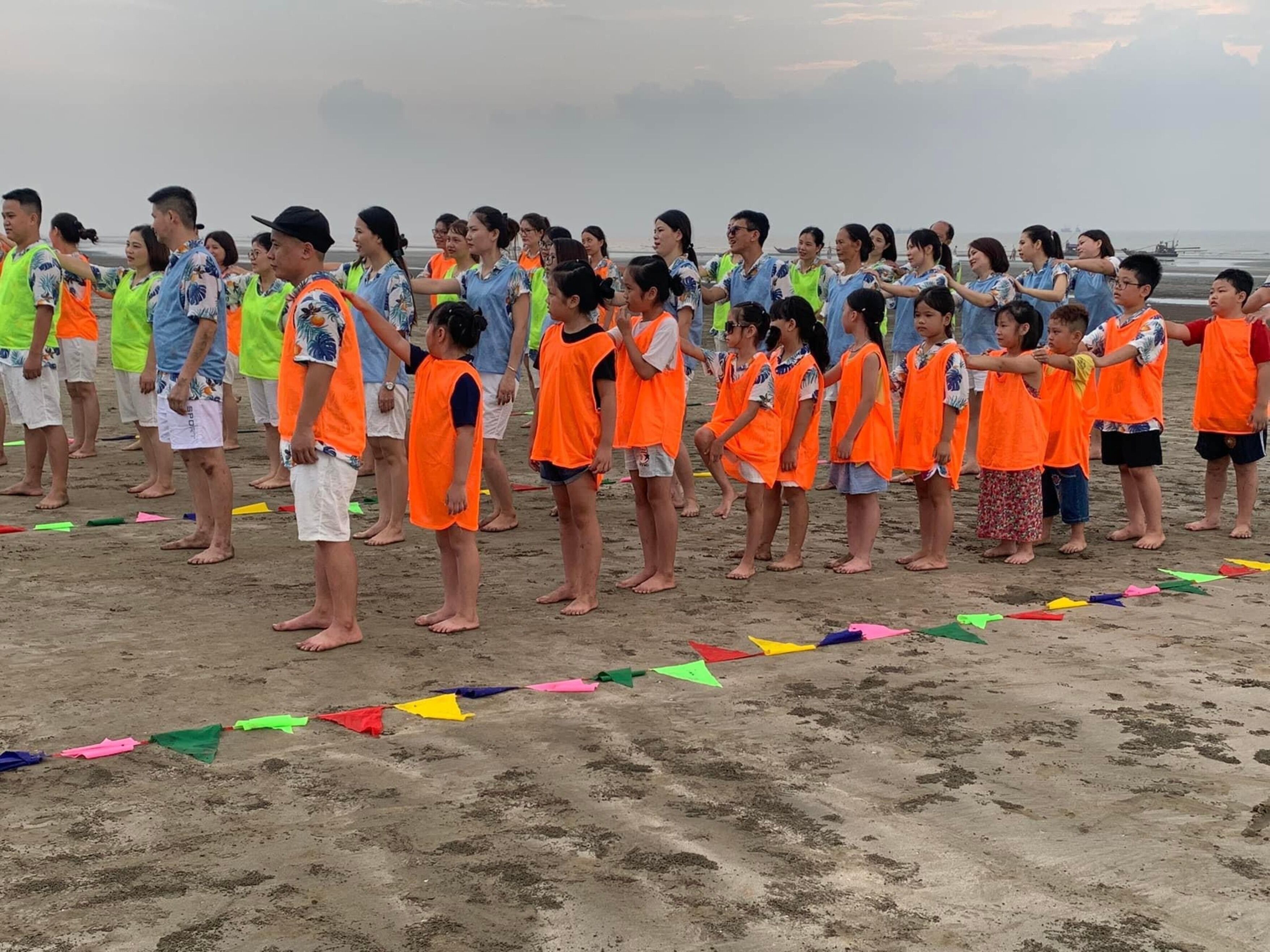 A group of people standing on a beach, some wearing orange vests.