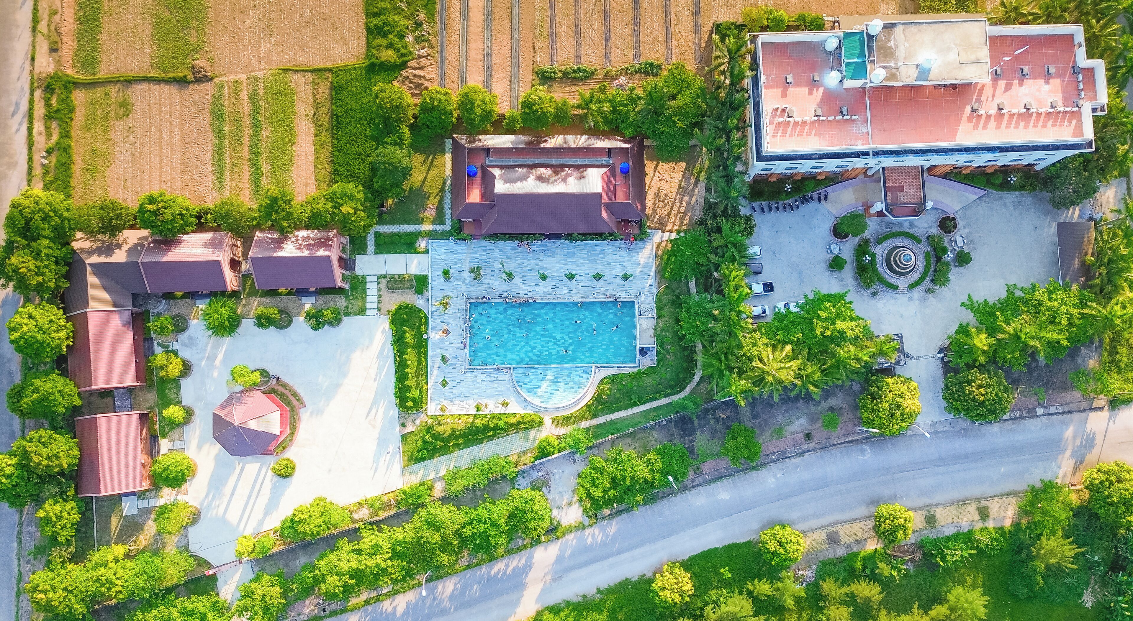 An aerial view of a resort with a swimming pool, multiple buildings, and surrounding greenery.