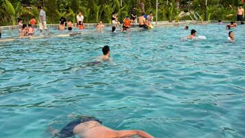 A swimming pool with people in the water, surrounded by greenery and a clear sky.