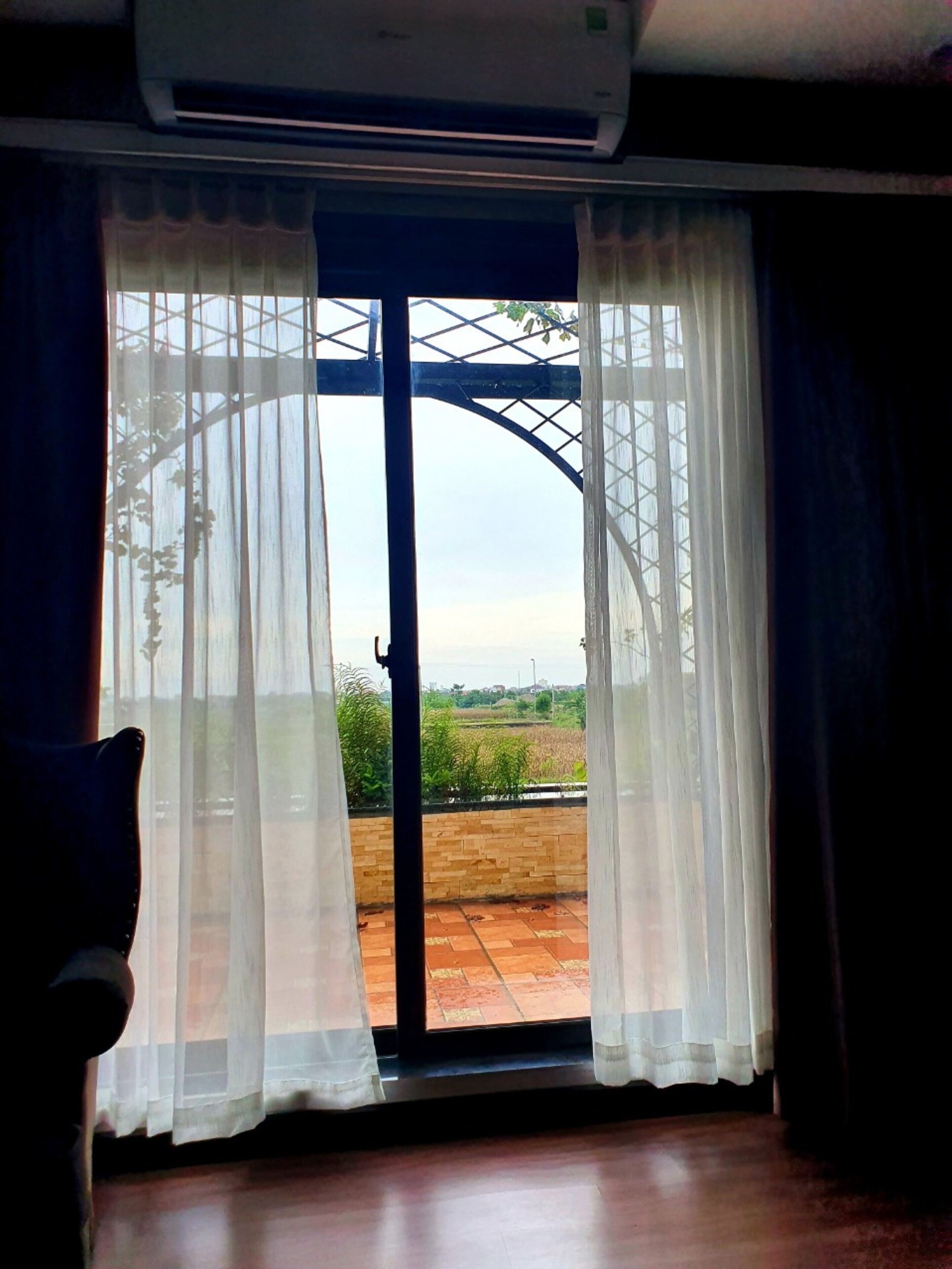A room with a large sliding glass door leading to an outdoor area with a view of greenery and a metal structure.