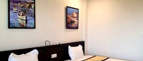 Habitación de hotel con dos camas, cada una con cubrecama blanco y cabecero marrón. Hay dos cuadros en la pared: uno muestra un barco en el agua y el otro, un paisaje.