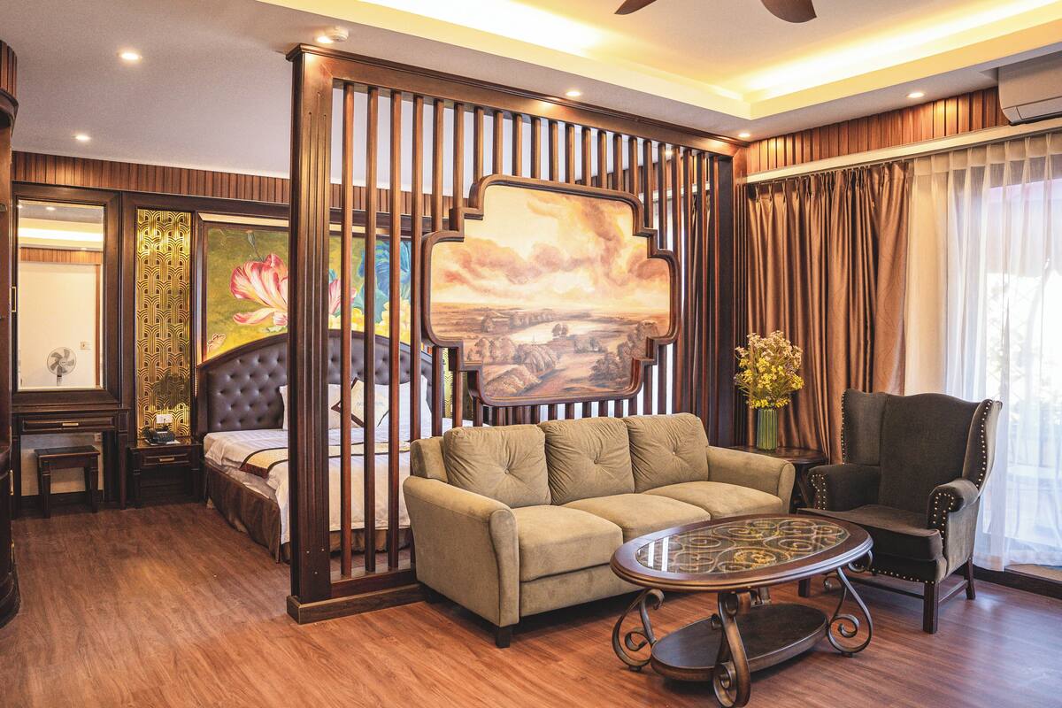 A living room with a sofa, armchair, and coffee table. There is a painting on the wall and a vase with flowers on a side table.