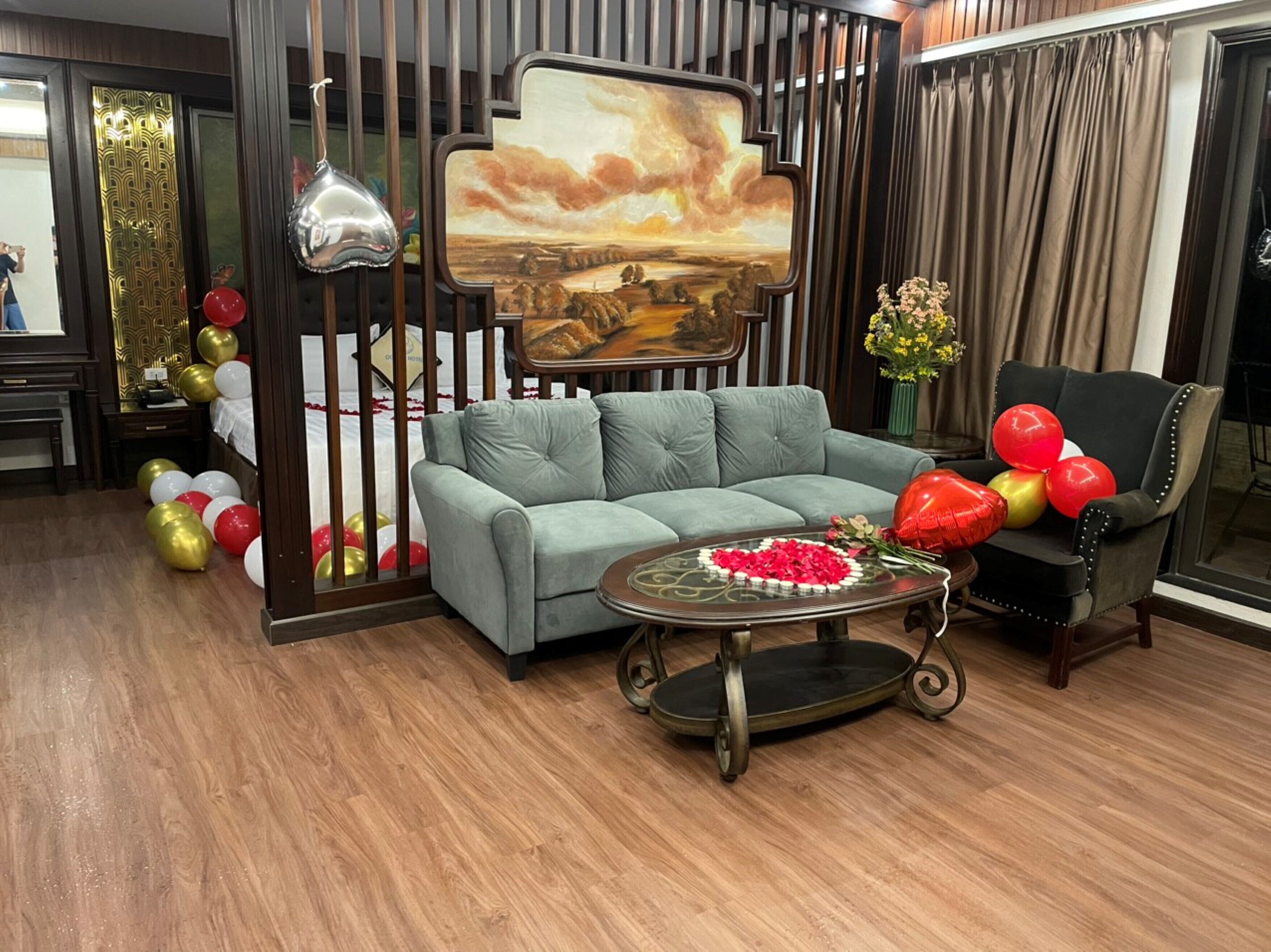 A room with a grey sofa, a coffee table with a floral arrangement, and a decorative wall panel with a landscape painting.