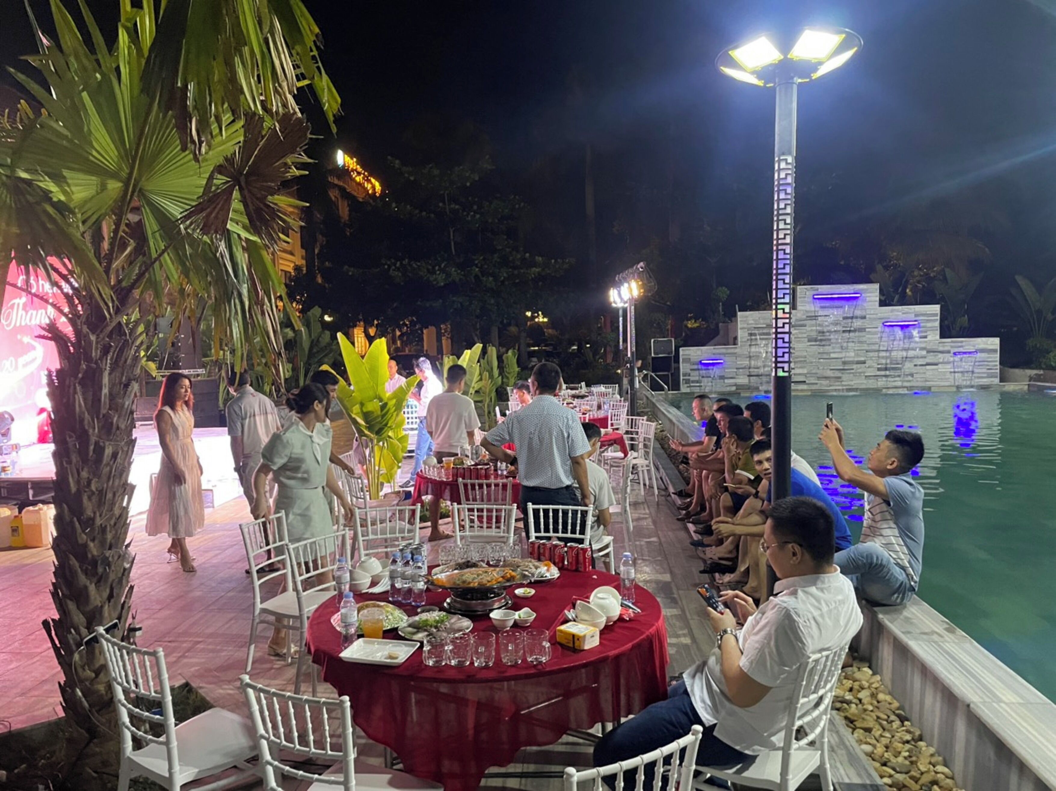 An outdoor dining area with round tables covered in red tablecloths, surrounded by white chairs.