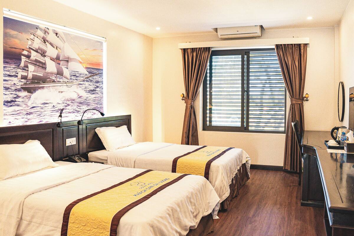 A hotel room with two beds, a large window with blinds, a flat-screen TV, and a poster of a ship on the wall.