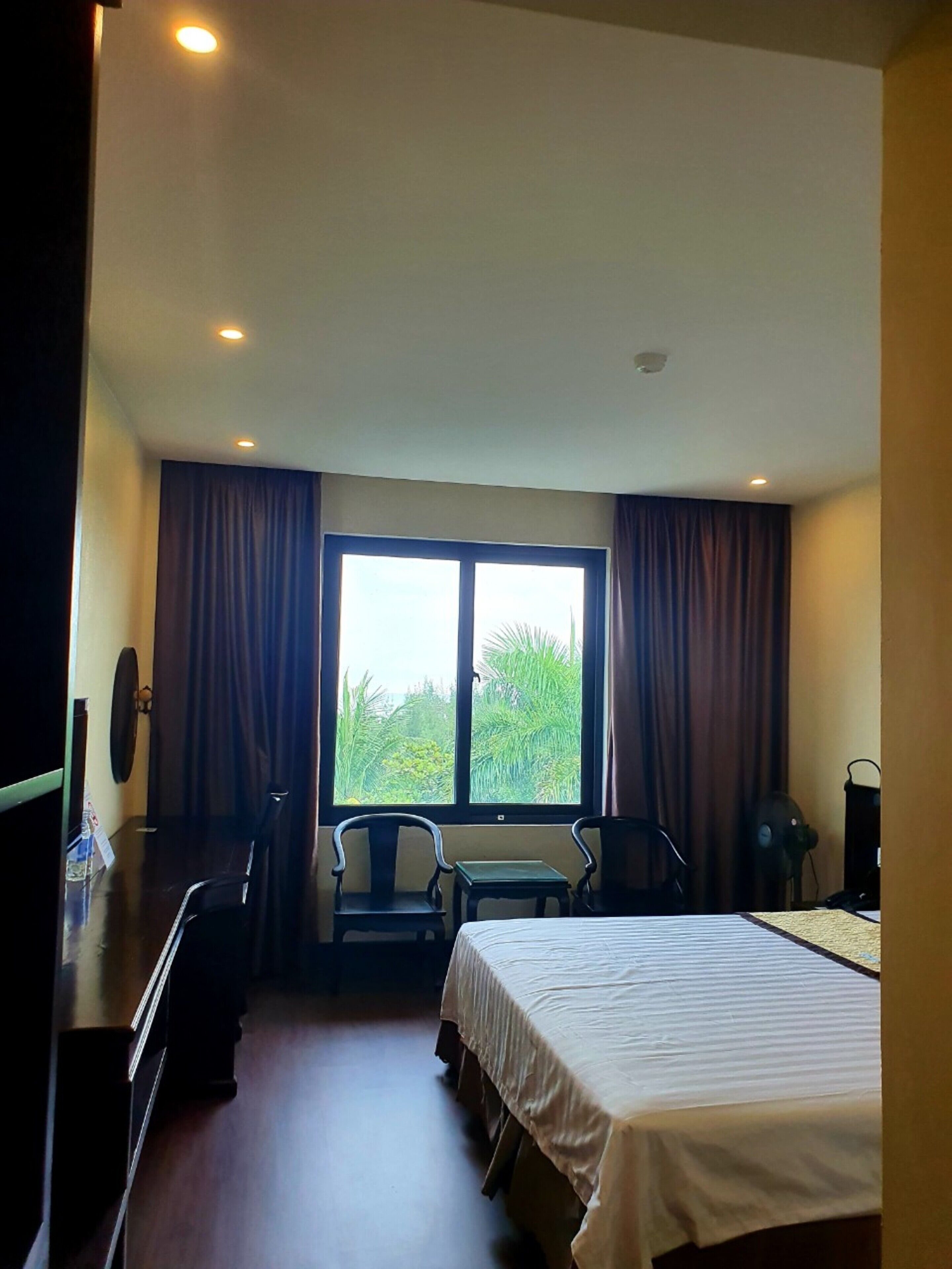 A hotel room with a bed, two chairs, a desk, and a window with curtains.