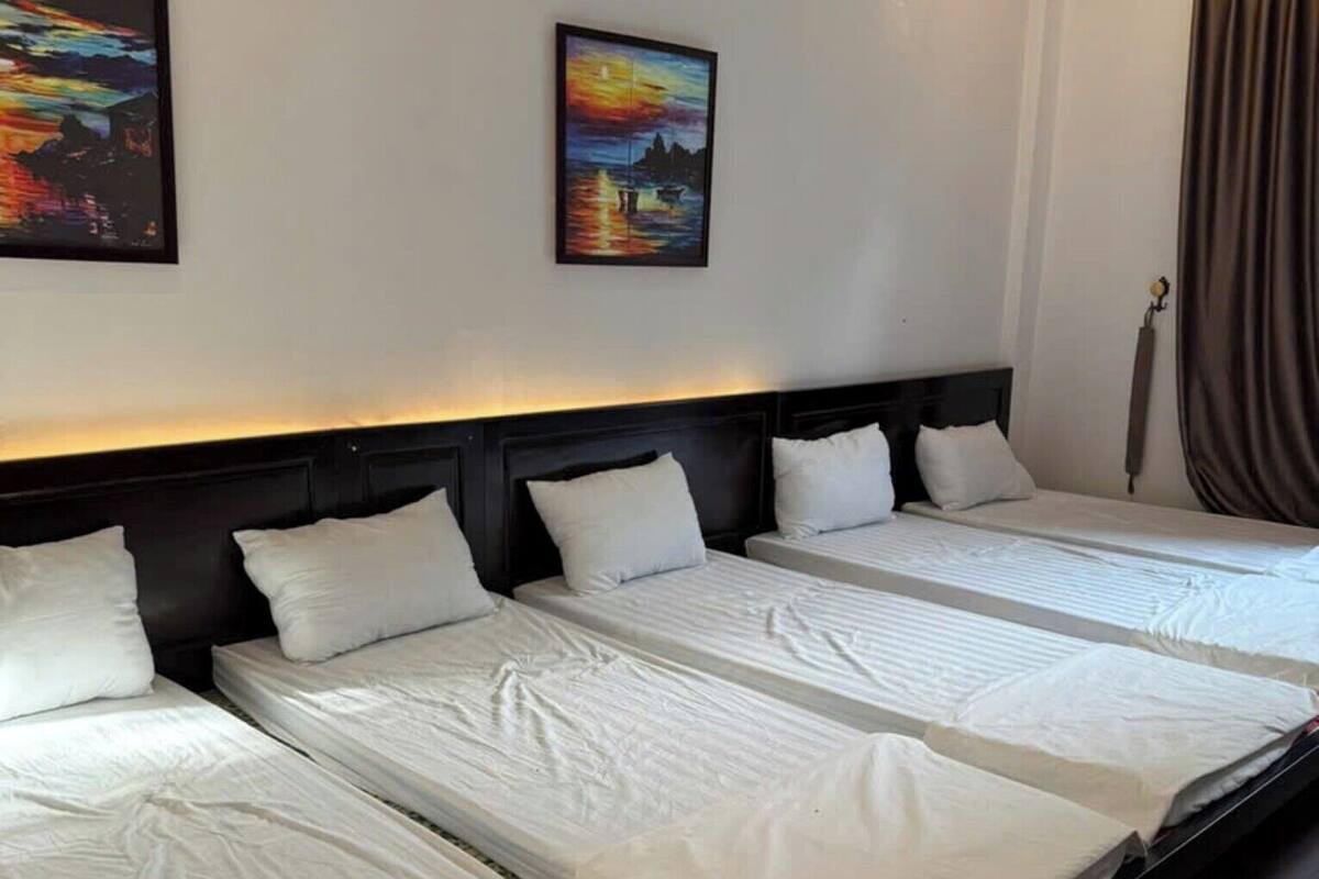 A hotel room with a large bed, a headboard, and two paintings on the wall.