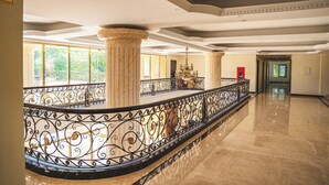Un pasillo amplio con suelo de mármol, barandilla de hierro ornamentada y grandes columnas.
