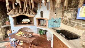 A rustic kitchen with a stone wall, a built-in oven, a wooden table with a bowl of fruit, and a gas stove. - Li Funnesi Villa sleeps 4, 2 bathrooms, A.C and large garden in San Teodoro (San Teodoro)